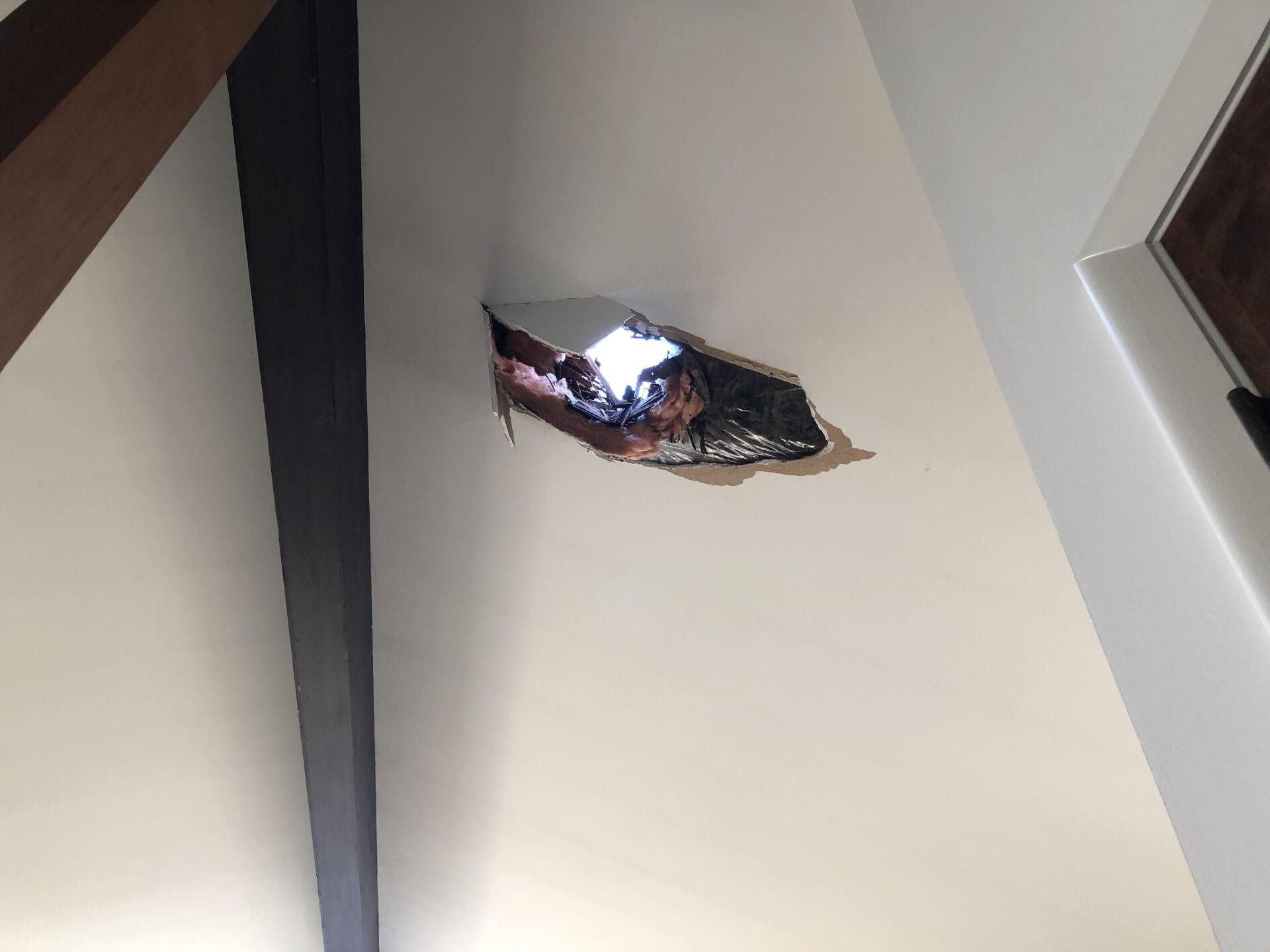 Damaged ceiling with a hole exposing debris and daylight inside a room