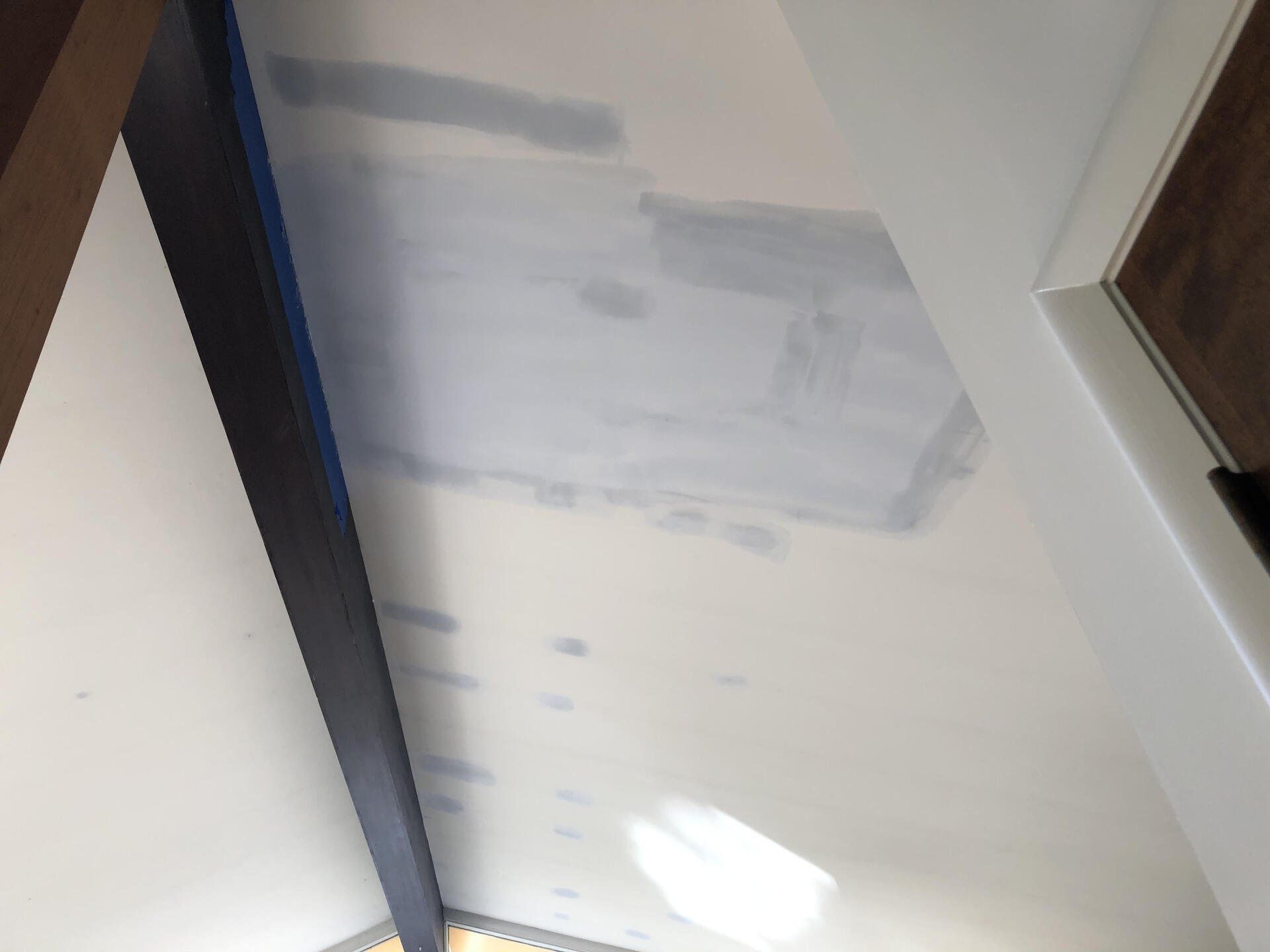 Partially painted white wall with gray primer patches in a hallway or stairwell