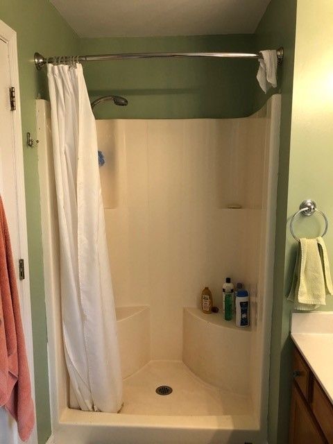 Small bathroom with a white shower stall, green walls, and a towel hanging beside a vanity.