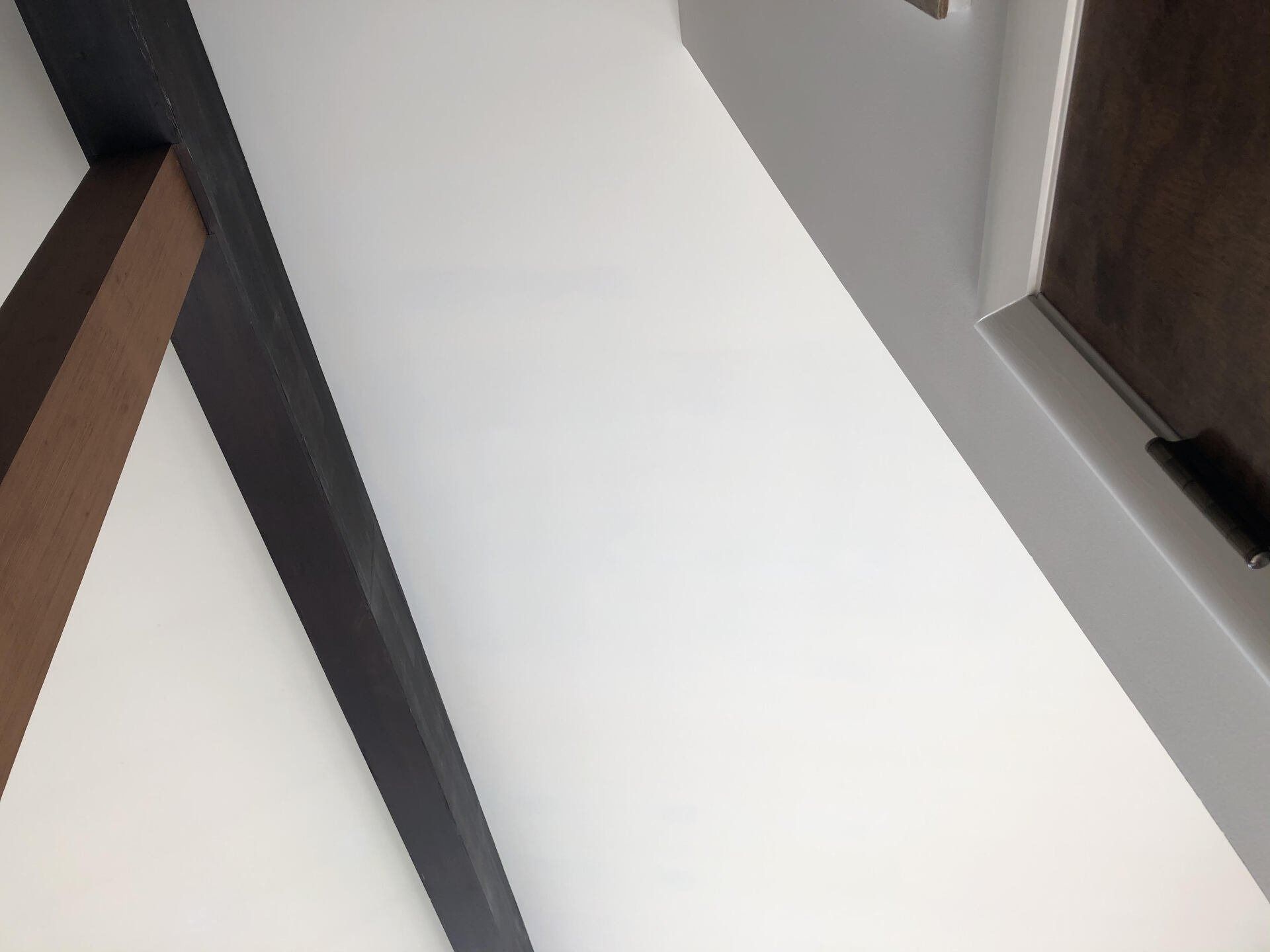 Empty hallway with white walls, dark wood trim, and a light floor seen from a tilted angle