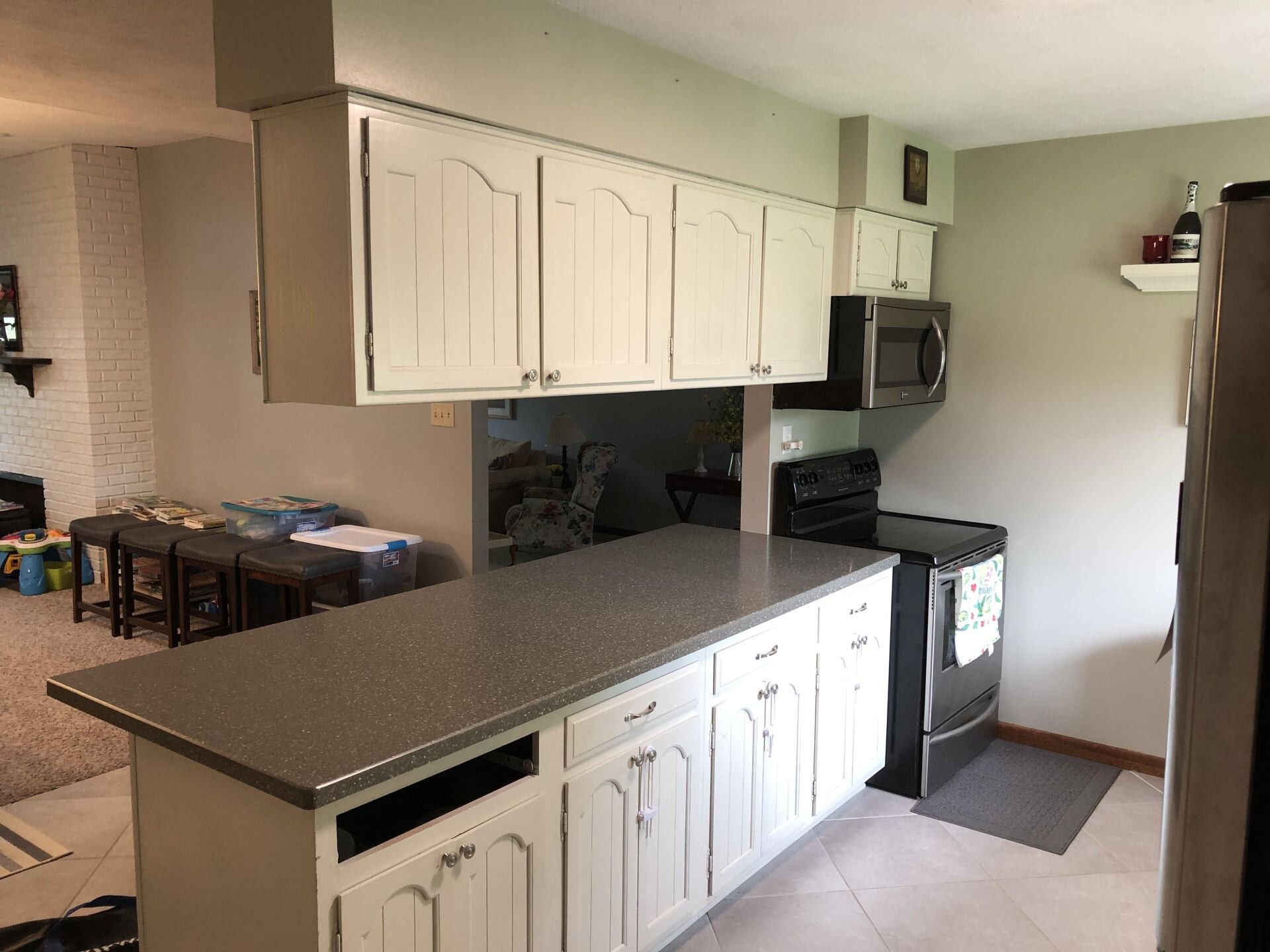 Kitchen with white cabinets, black countertops, and a stove beside a breakfast bar.