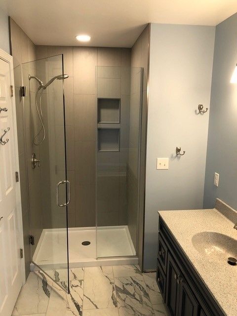 Modern bathroom with glass walk-in shower, tiled walls, and vanity sink under a mirror.