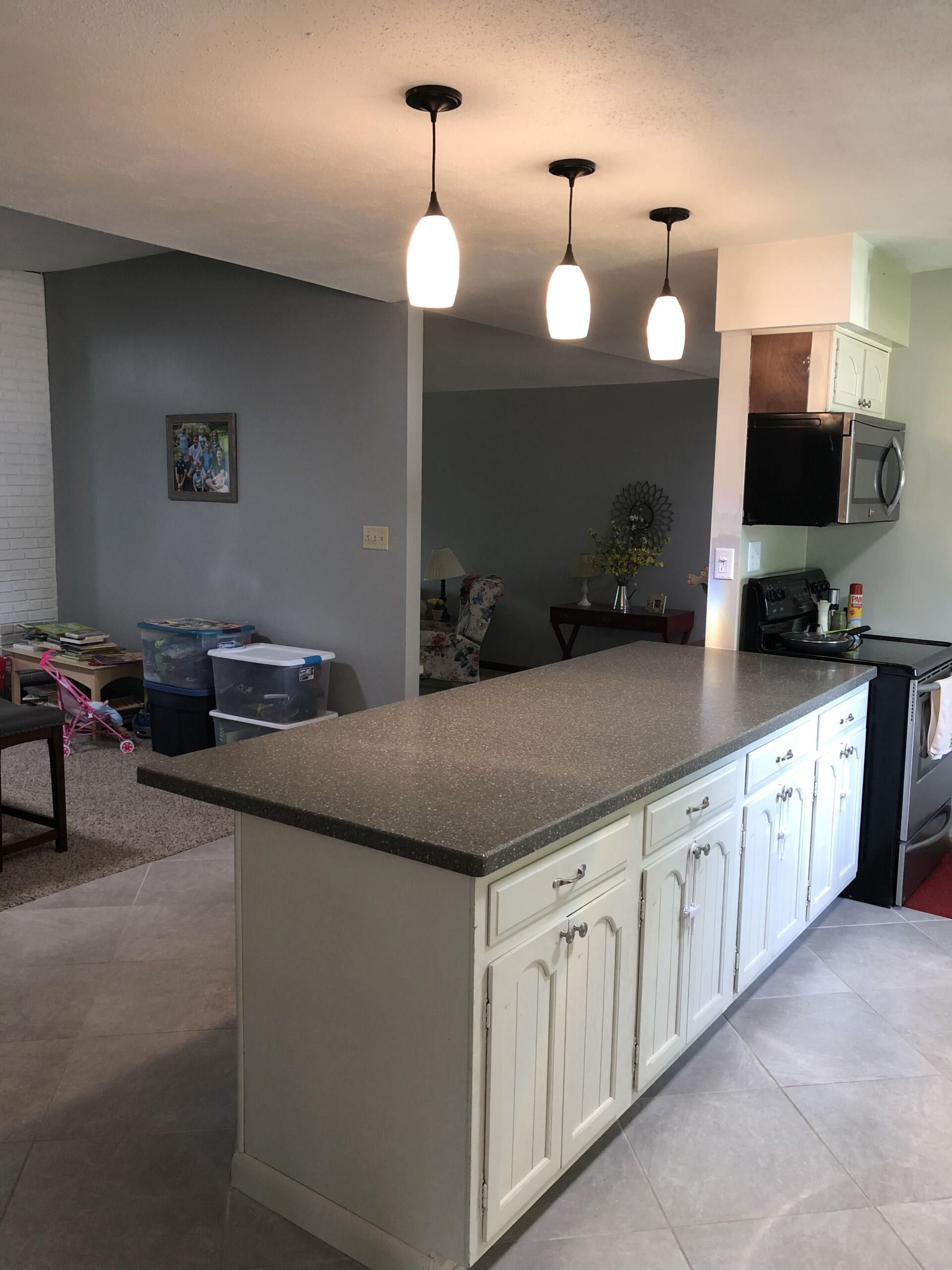 Kitchen island with granite countertop, white cabinets, and three pendant lights in an open living space
