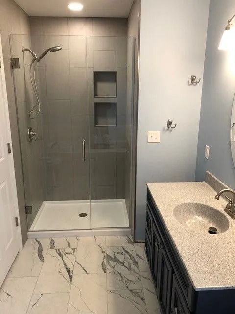 Modern bathroom with glass shower, marble floor, and dark vanity with sink