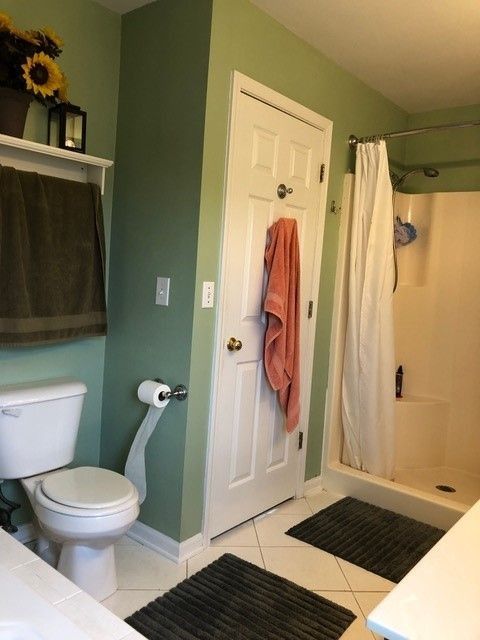Green bathroom with shower, toilet, sink, and towels hanging on the door