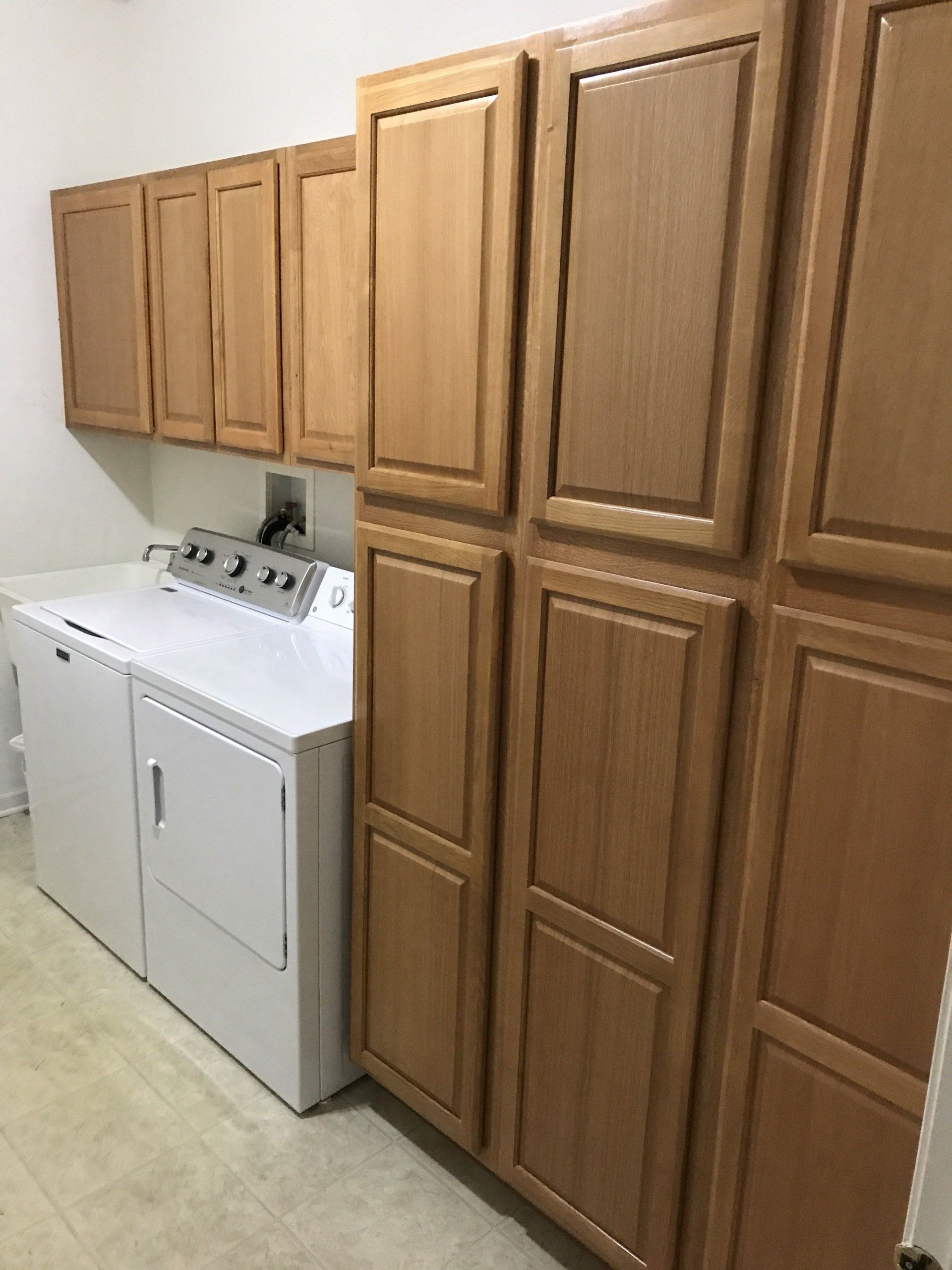 Laundry room with white washer and dryer beside tall oak cabinets.