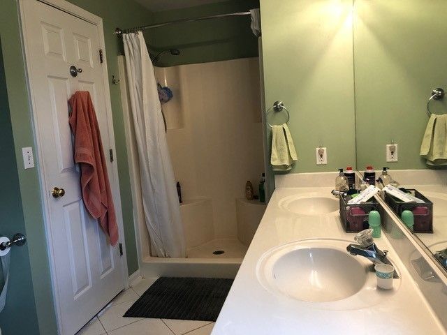 Bathroom with green walls, white vanity, mirror, shower curtain, and towels hanging on the door