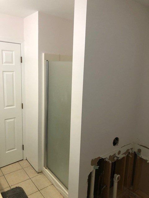 Partially renovated bathroom with white shower door, tiled floor, and exposed wall studs near a doorway