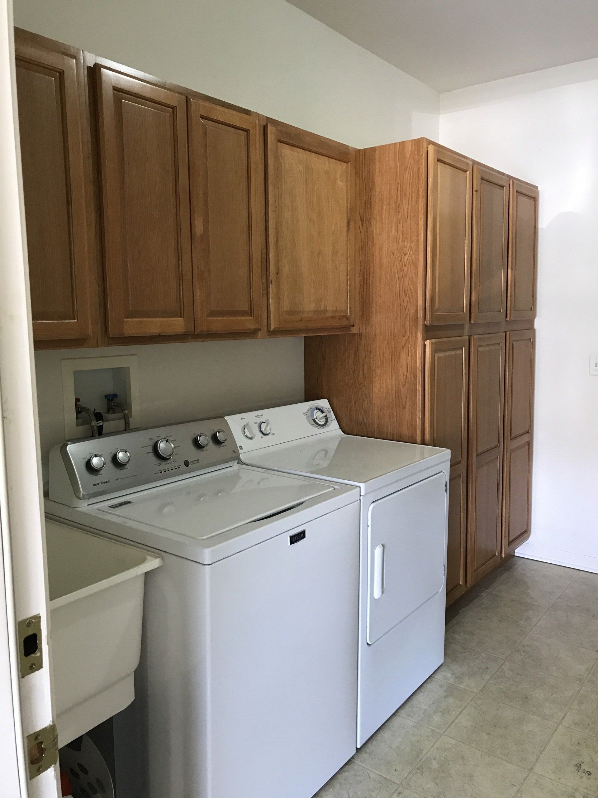Laundry room with white washer and dryer, wood cabinets, and a utility sink.