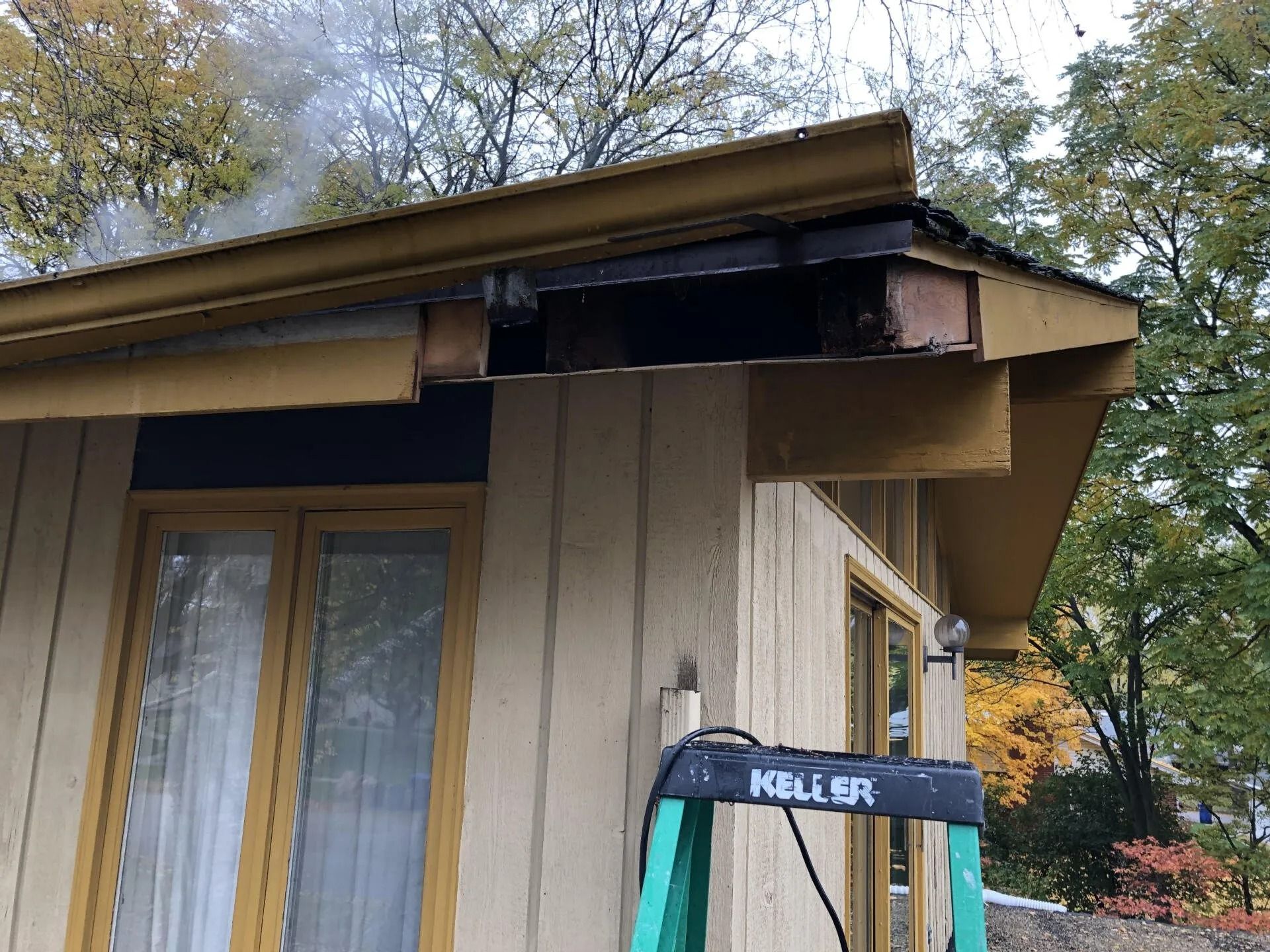 Damaged house roof with missing fascia and exposed wood, with a ladder in front