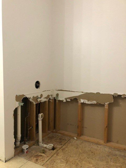Damaged wall with exposed studs and plumbing in a room under renovation