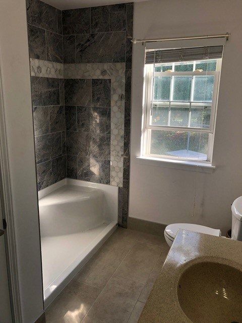 Small bathroom with tiled shower, white tub, window, and pedestal sink.