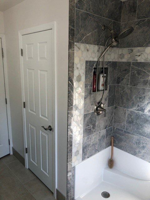 Bathroom shower with gray tile, white tub, and a nearby closed door