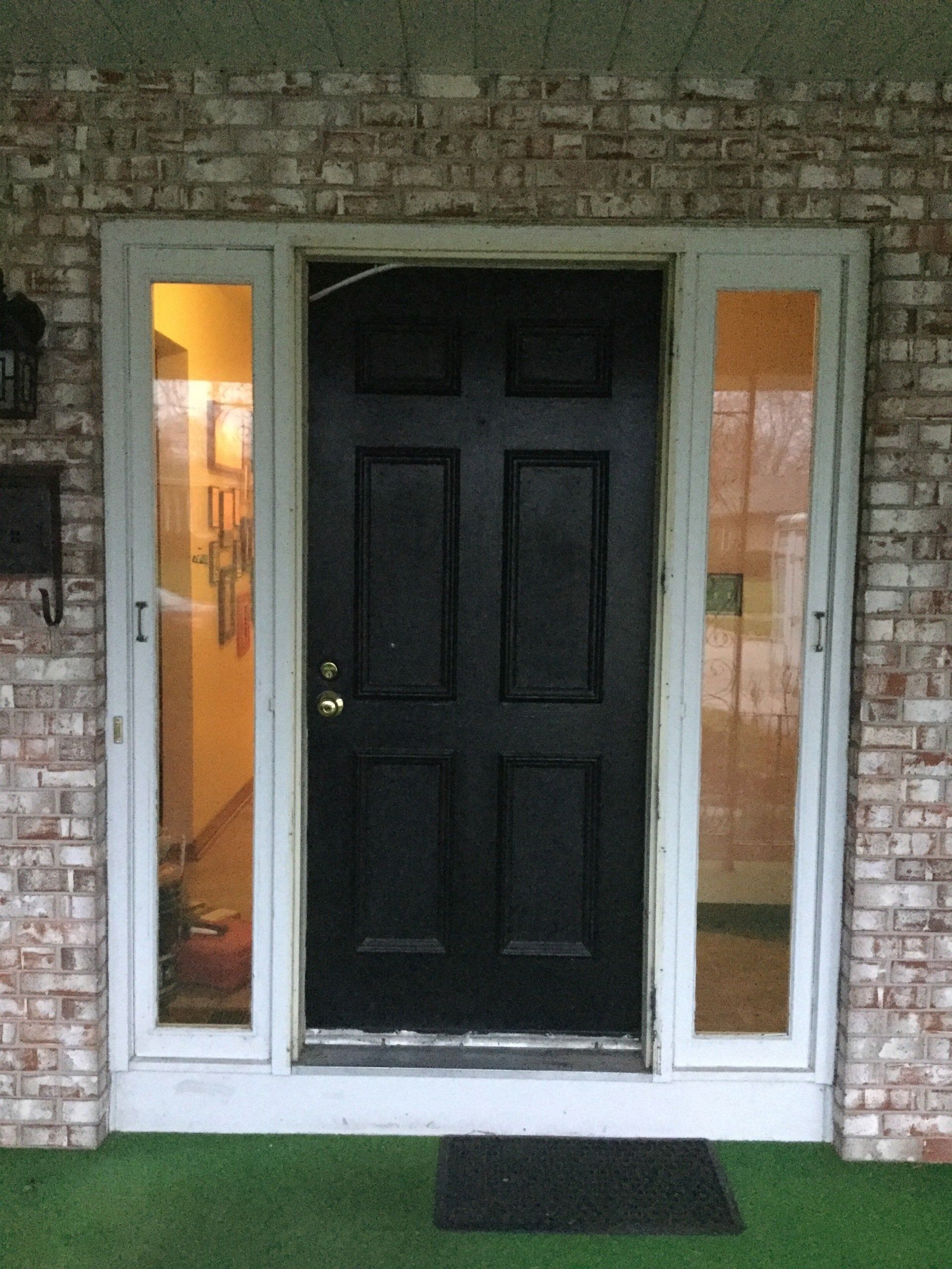 Front entrance with a black door, narrow side windows, and a doormat on a brick exterior