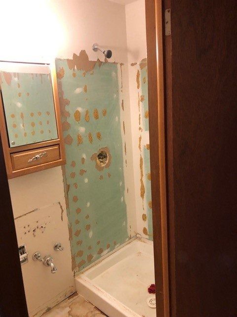 Small bathroom with teal shower curtain, beige tile walls, mirror cabinet, and sink area.
