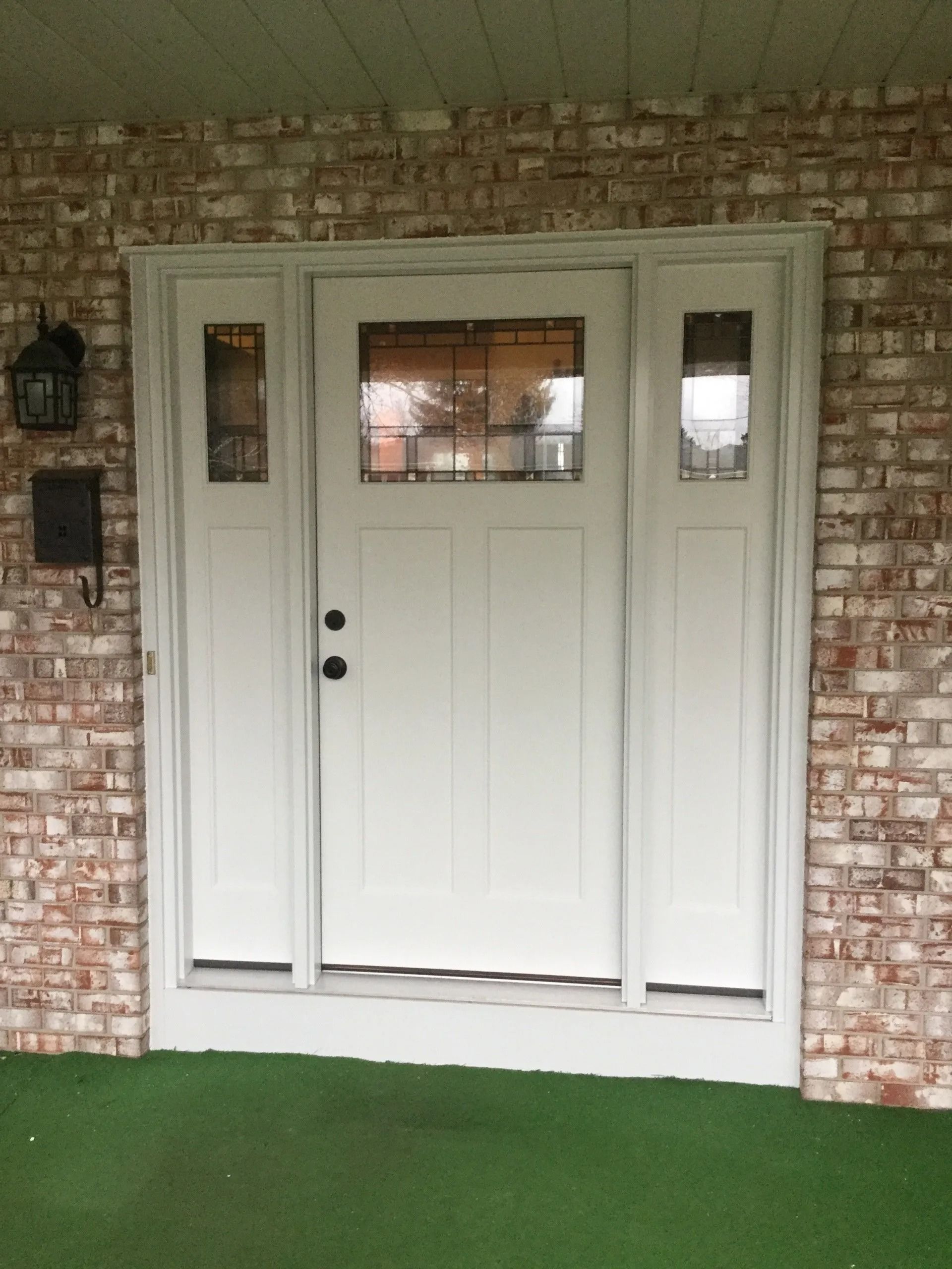 White front door with glass panes in a brick entryway and green carpeted porch