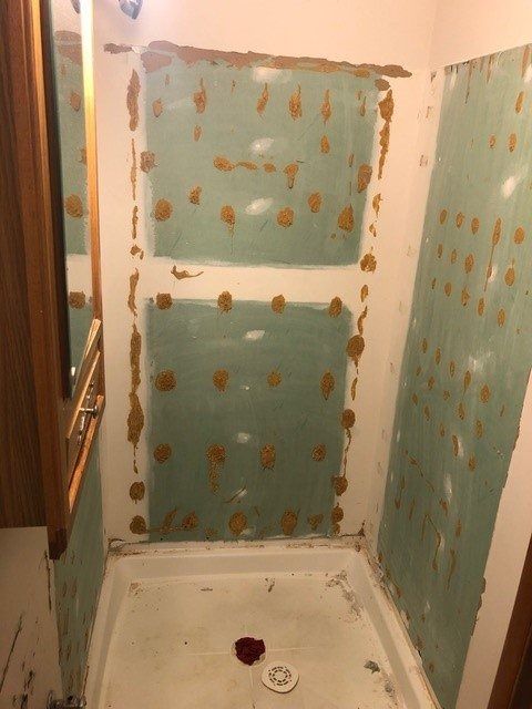 Small shower stall with blue-green walls covered in adhesive patches and a white floor pan.