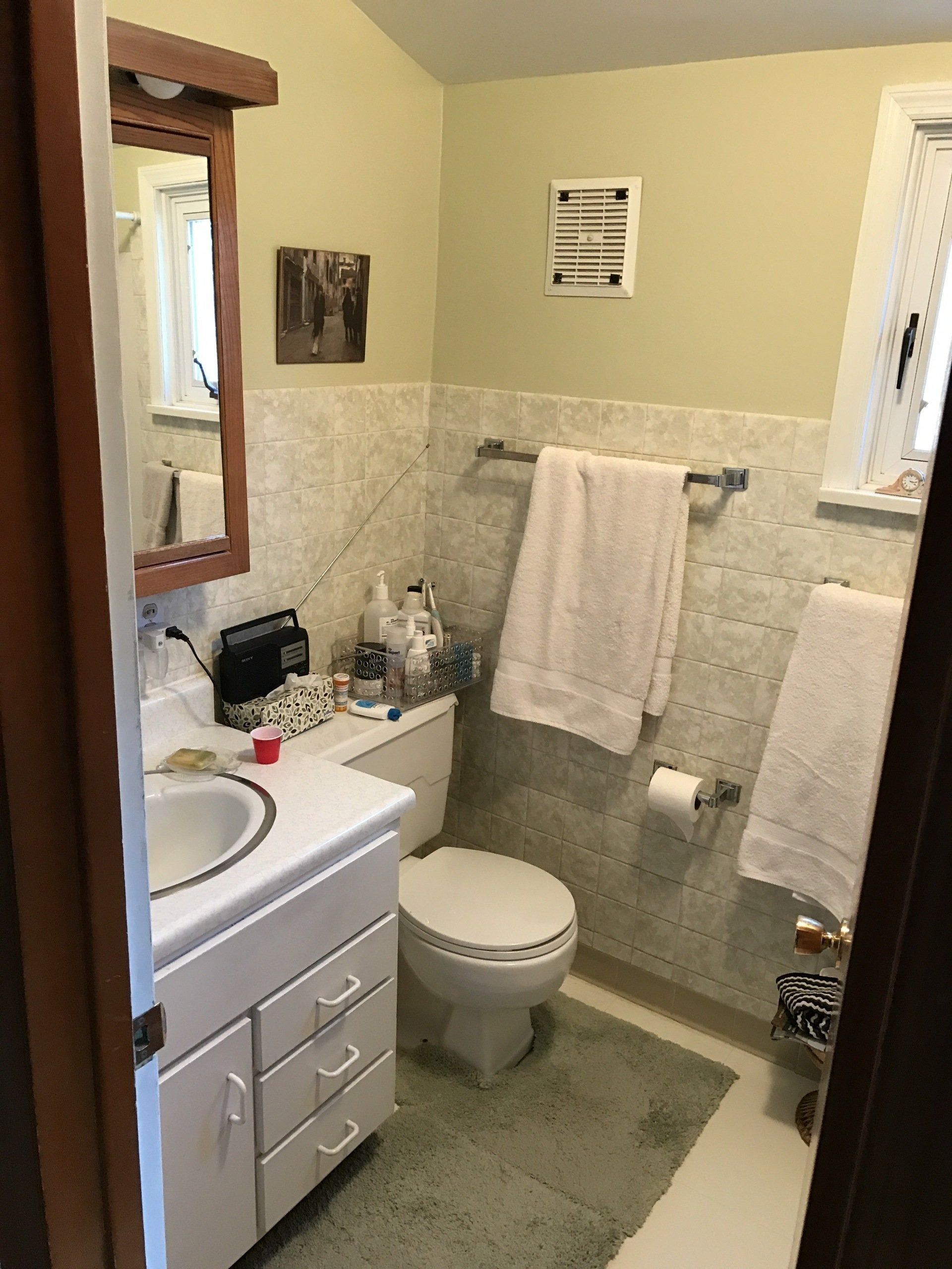 Small bathroom with sink, toilet, mirror, towel racks, and beige tile walls.