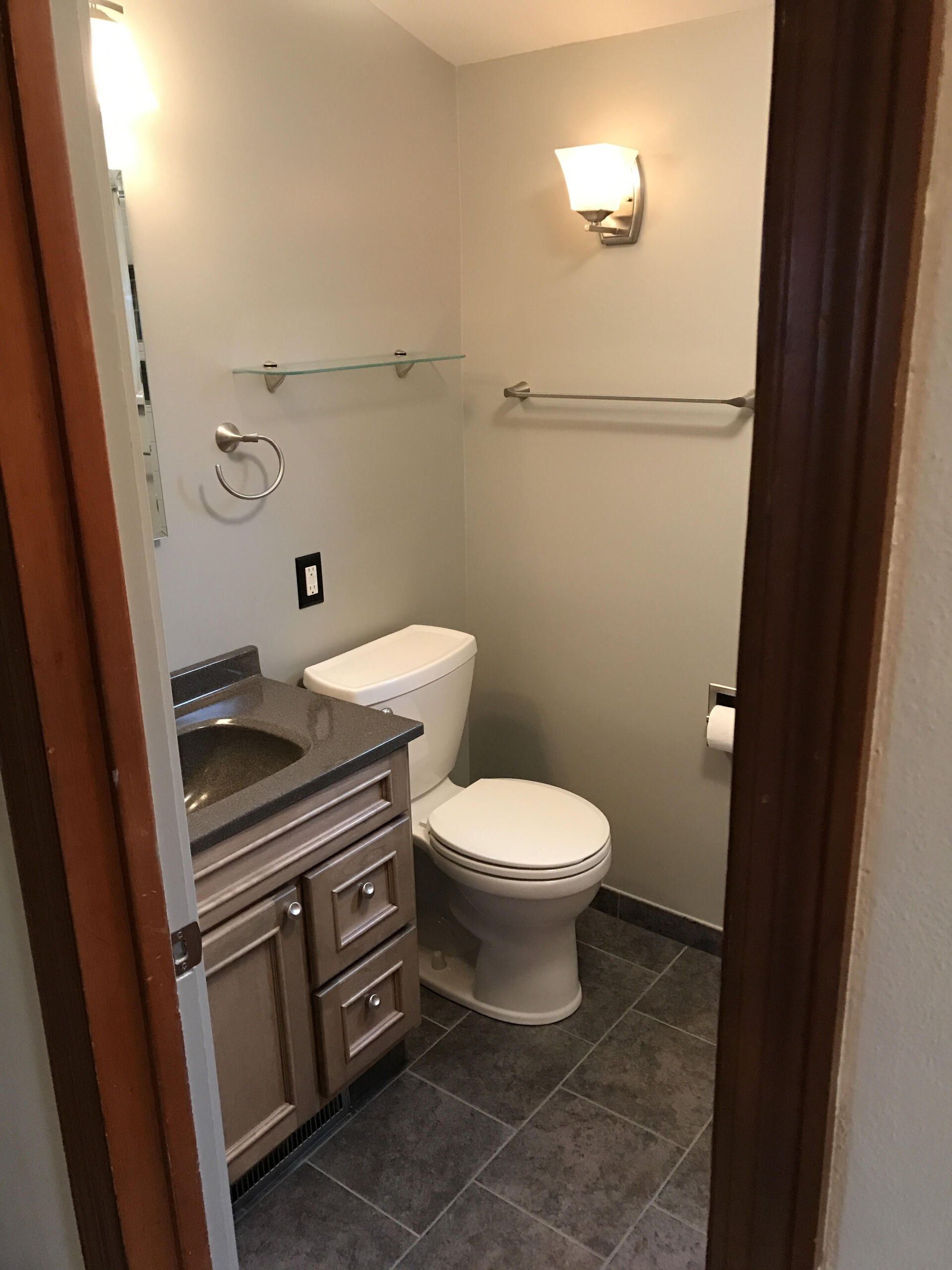 Small bathroom with toilet, dark vanity, wall sconce, and towel bars.