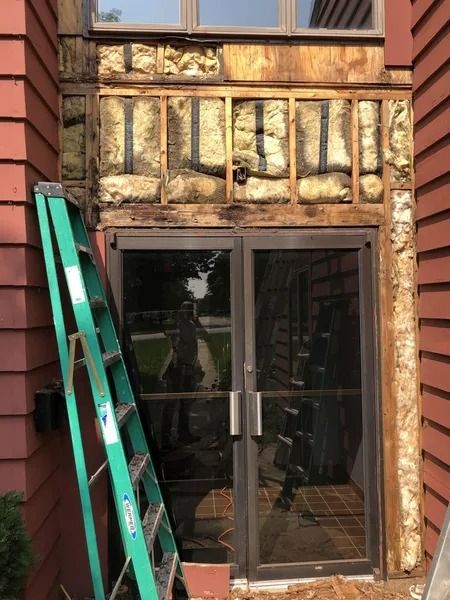 Exterior of a building with glass double doors and a green ladder leaning against the wall.