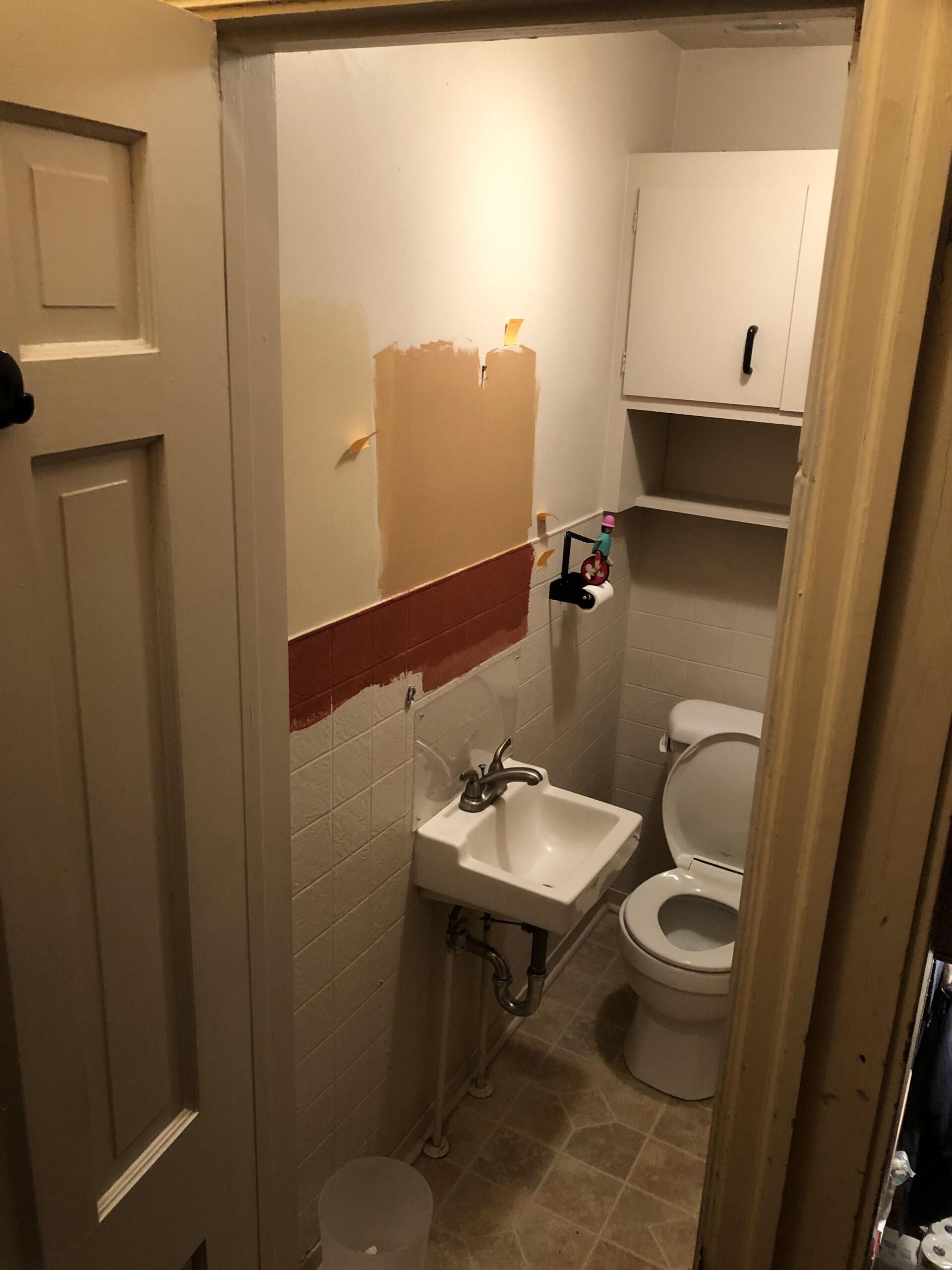 Small bathroom with sink, toilet, open cabinet, and damaged wall paint near the mirror area