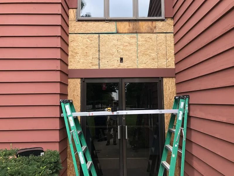 Ladders flanking a doorway beneath a tan balcony, between two red-sided buildings