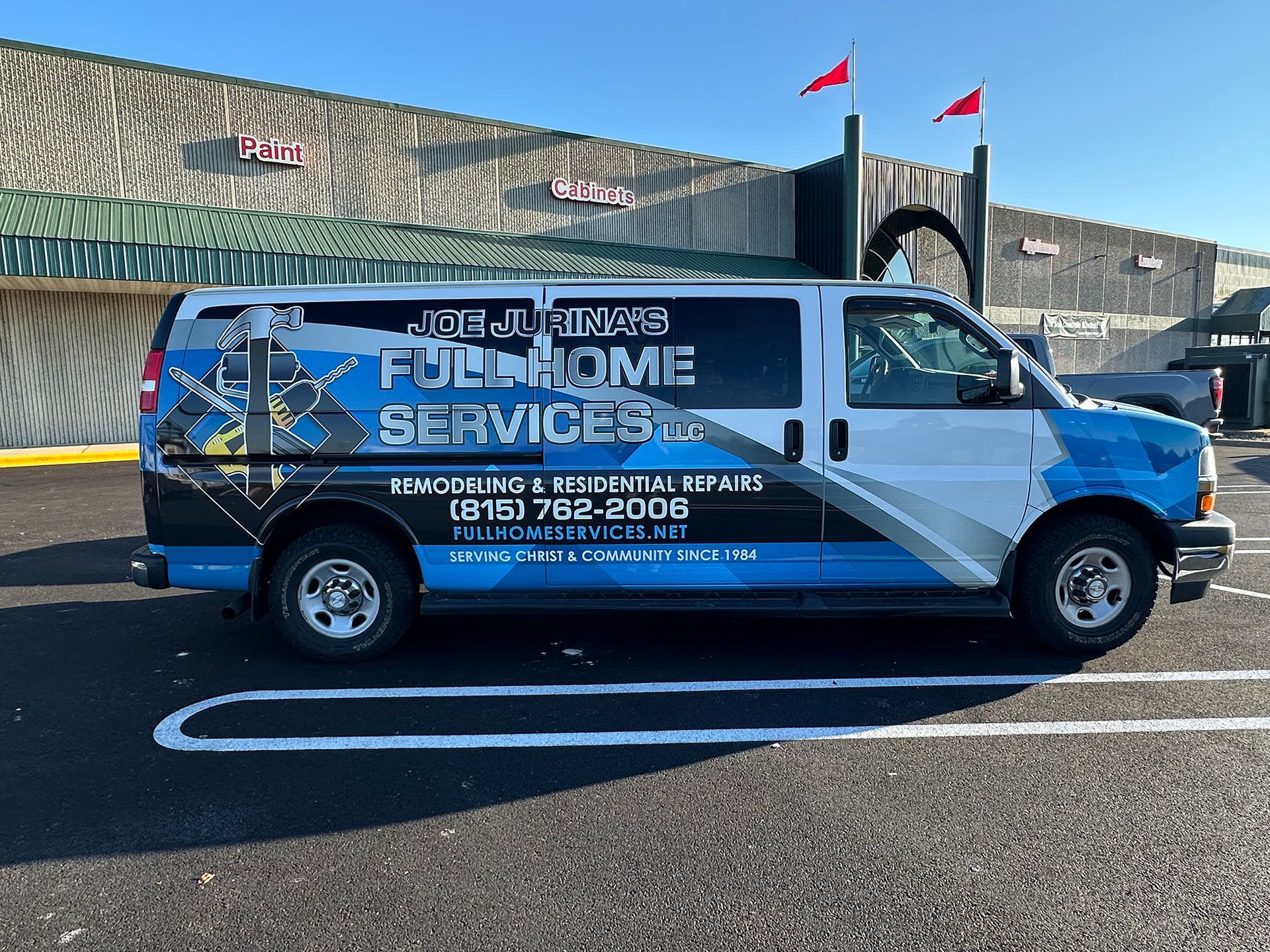 Blue customer service van parked by a stone wall with red flags, labeled “Home Service” on the side.