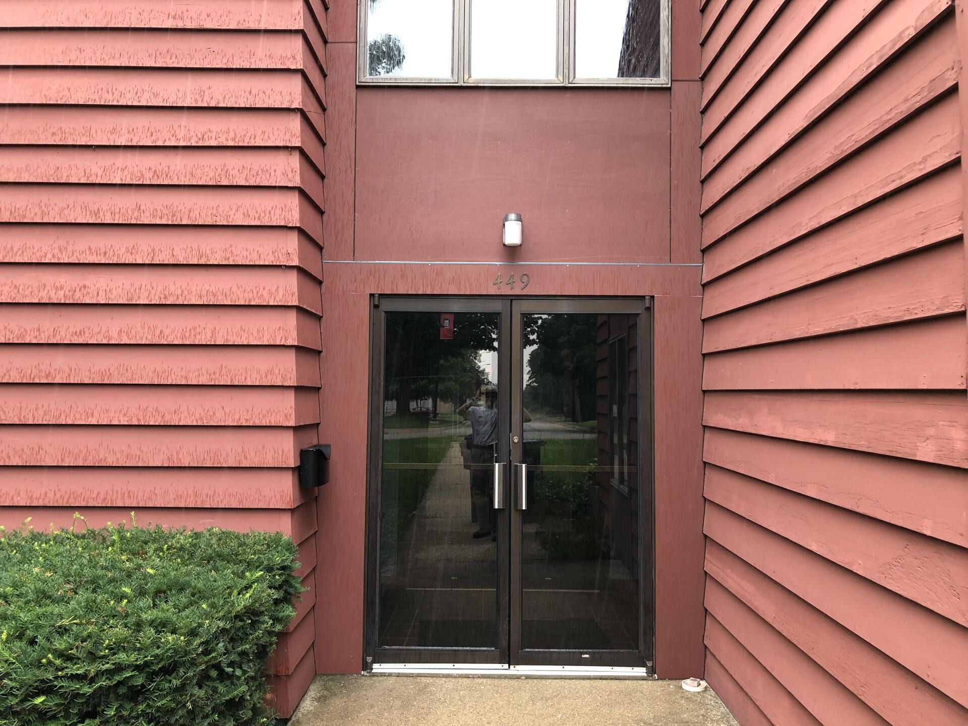 Glass double doors between red siding walls with a small light above the entrance.