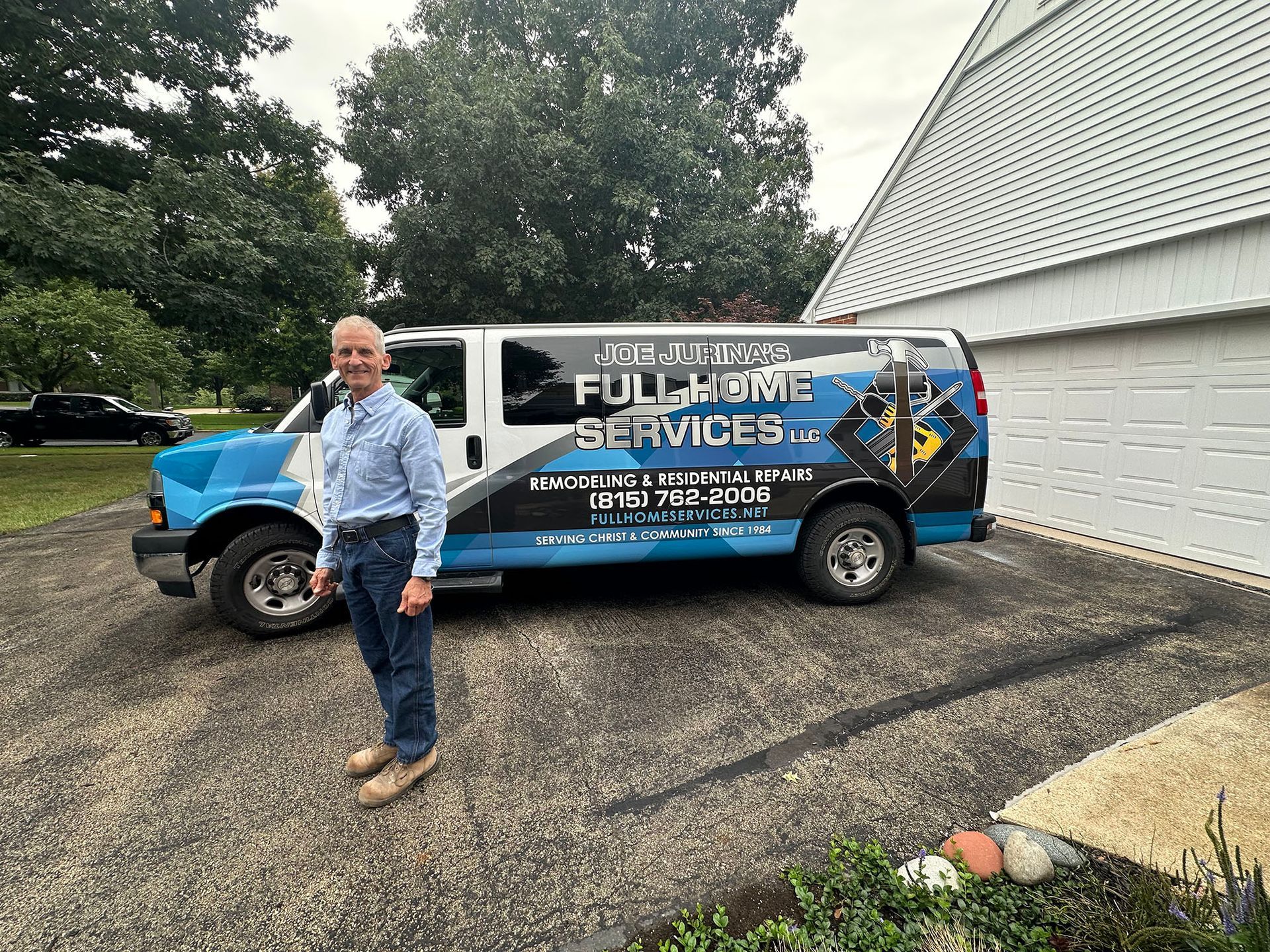 Man standing beside a blue Full Service van in a driveway outside a white house.