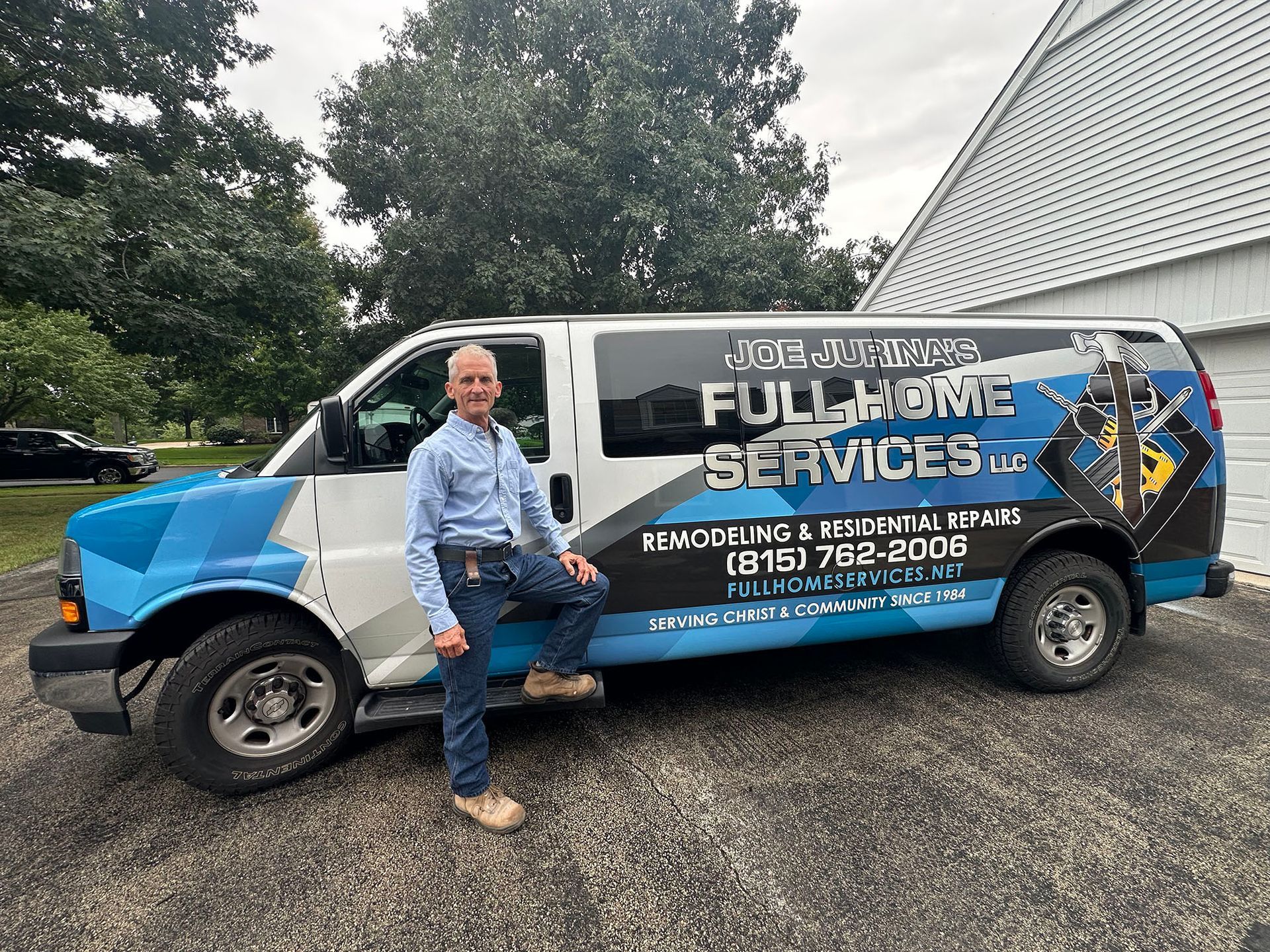 Man sitting on a blue-and-white service van with company logo in a driveway.