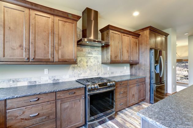 Modern kitchen with dark wood cabinets, granite counters, stainless range hood, and stove on a tiled floor