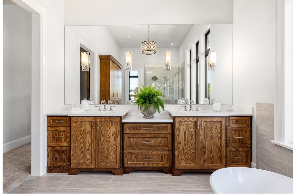 Elegant bathroom with carved wood vanity, white marble counters, mirrors, and a green floral centerpiece