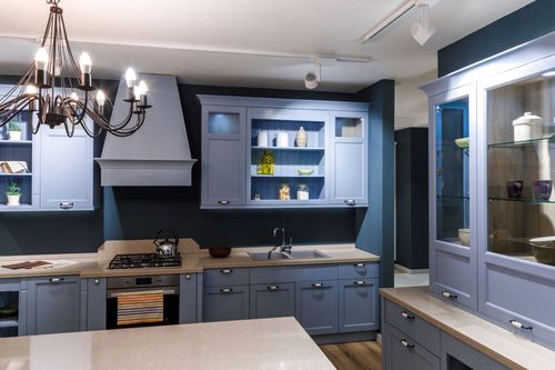 Blue kitchen with dark countertops, white island, chandelier, and glass-front cabinets