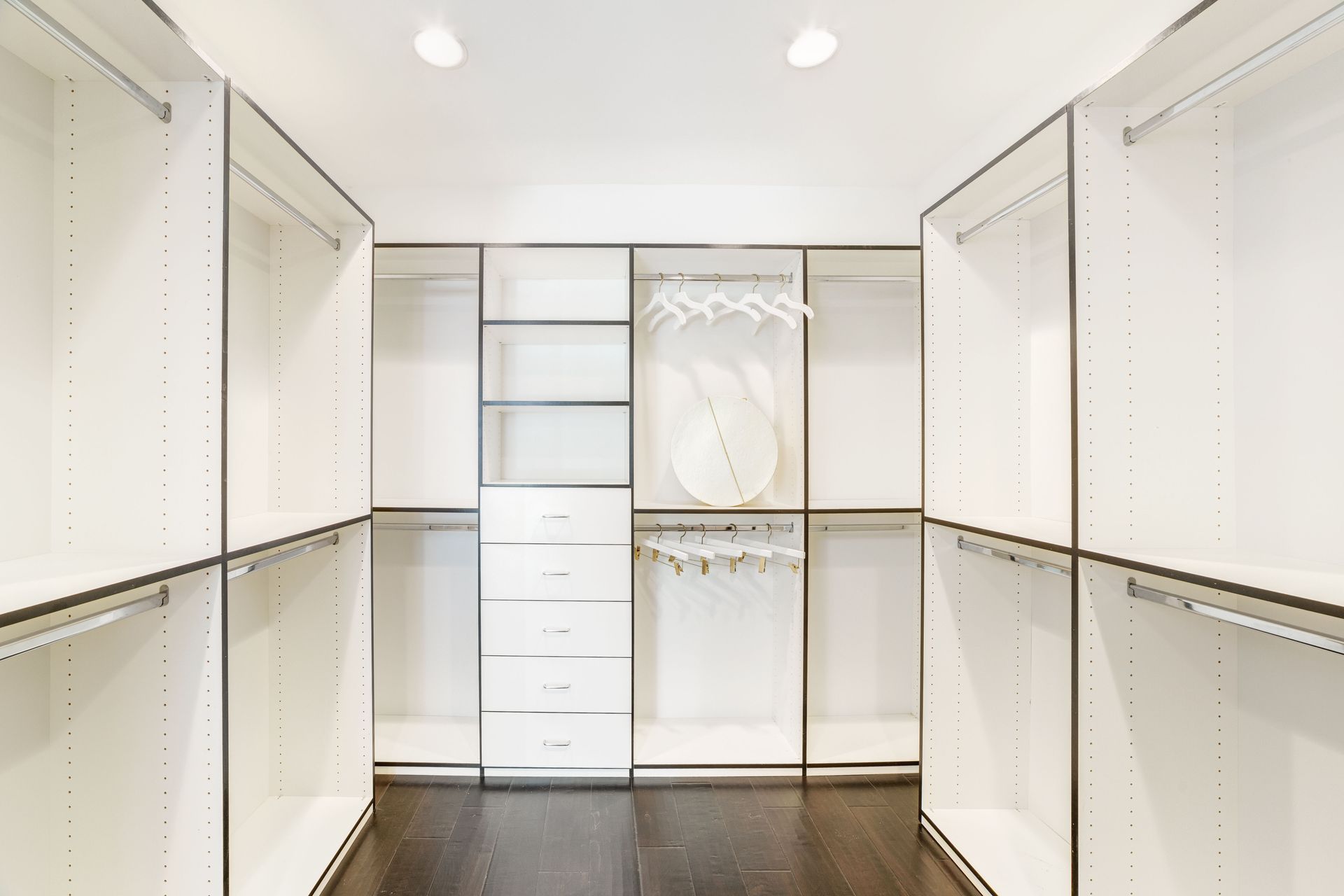 Bright white walk-in closet with shelves, drawers, hanging rods, and dark wood floor