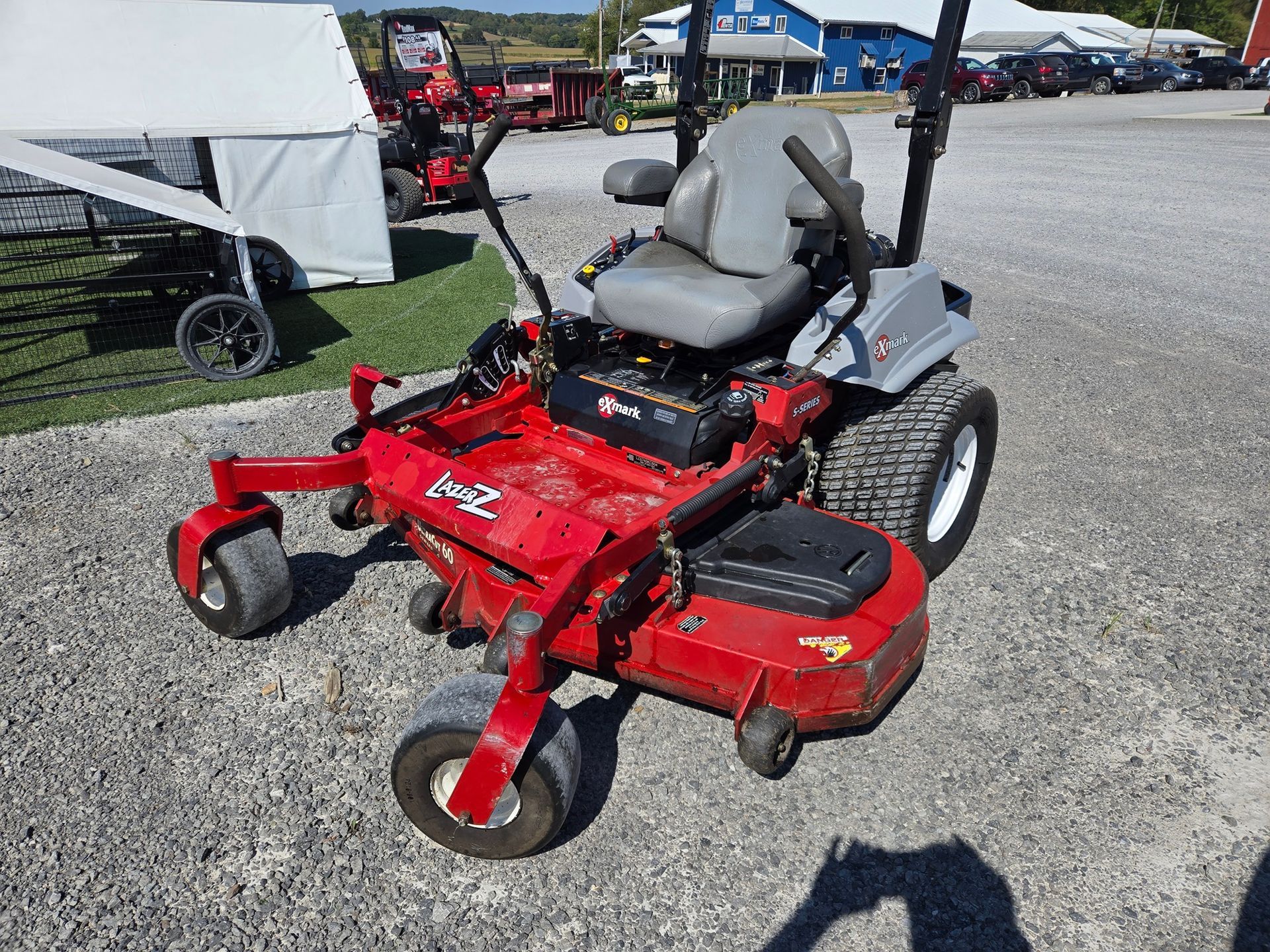 A red and black lawn mower is parked in a gravel lot.