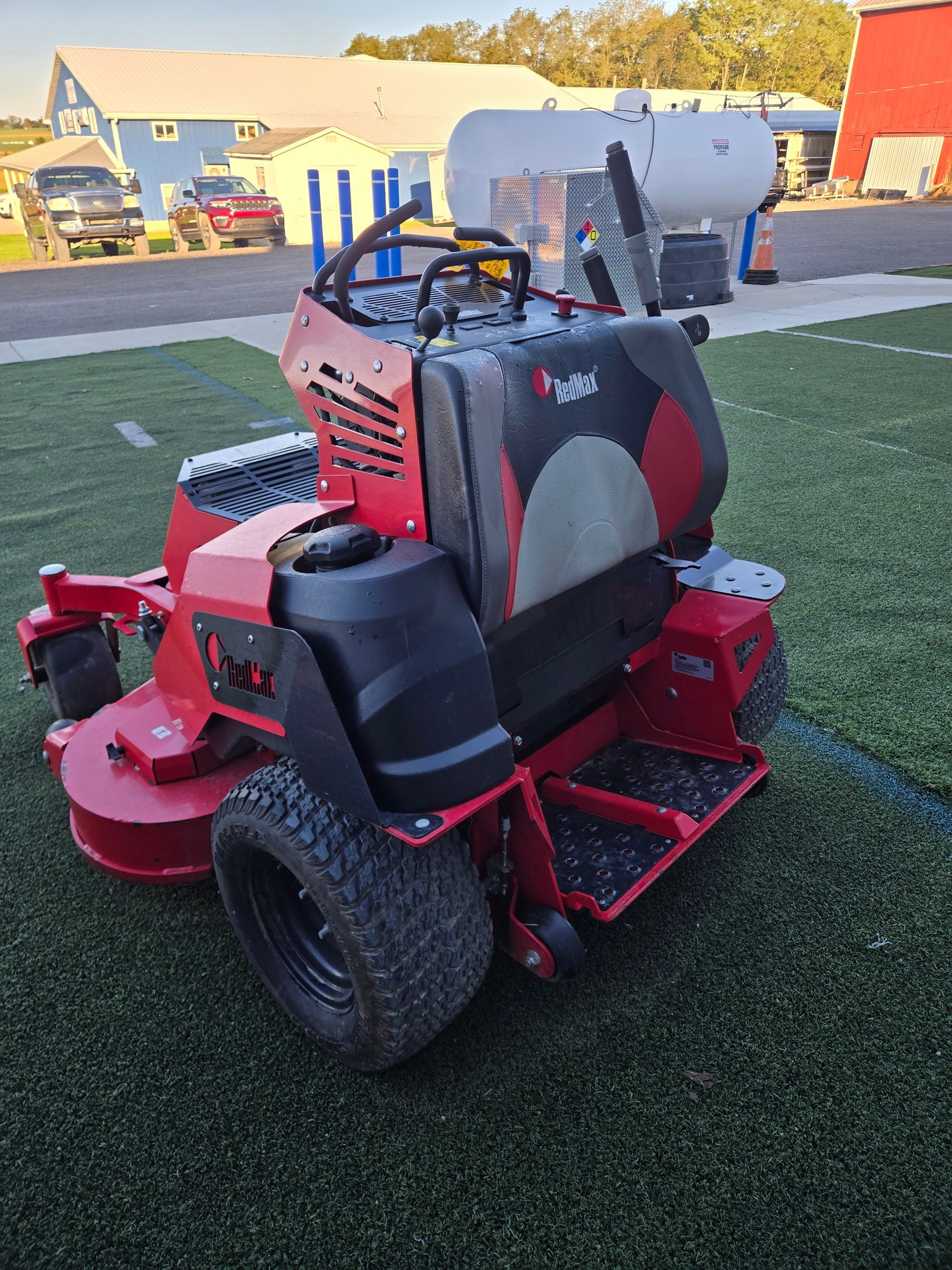 A red and black lawn mower is parked in a gravel lot.