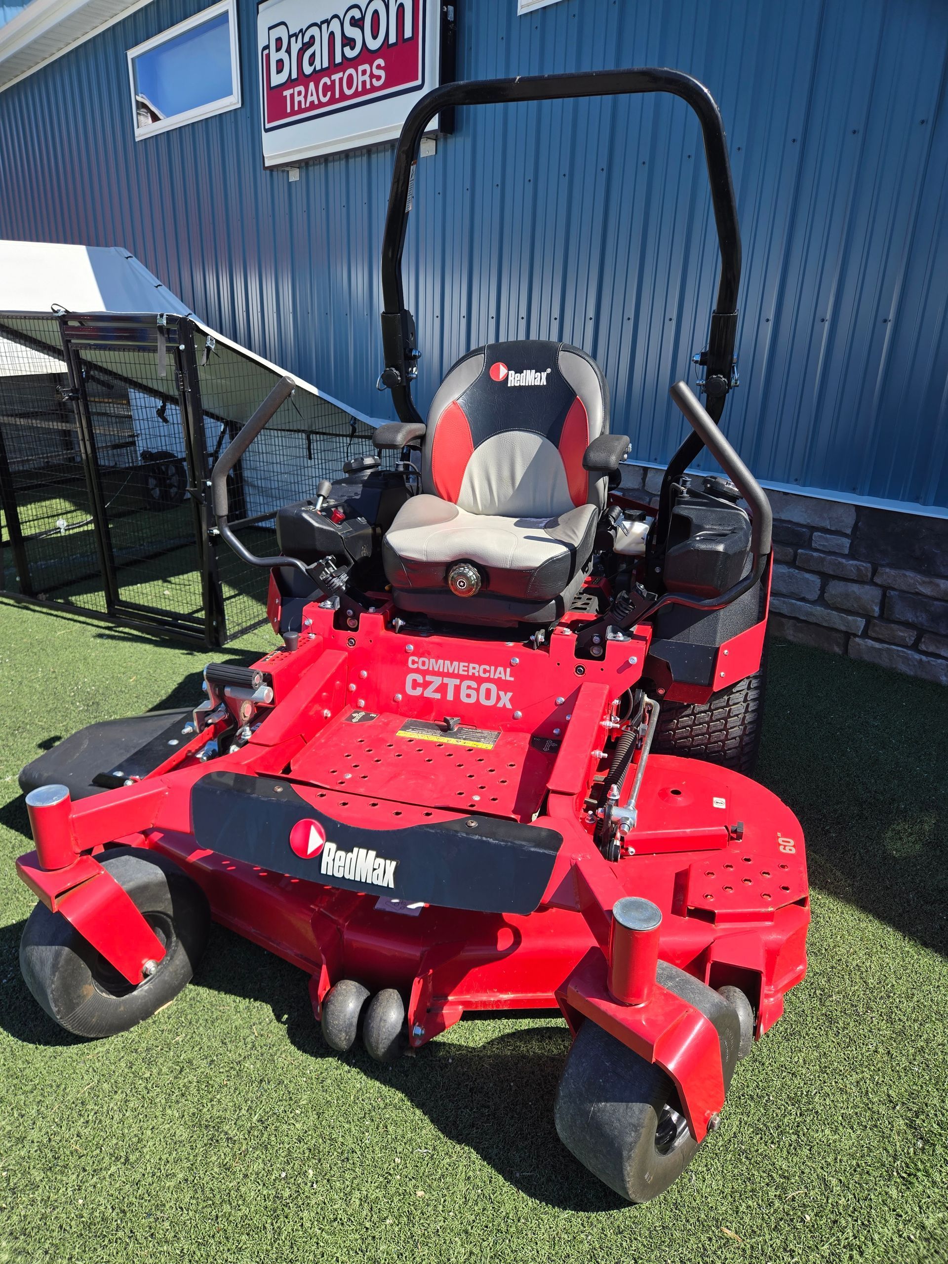 A red Bad Boy zero-turn mower with a black roll cage sits on synthetic turf in front of a blue building.