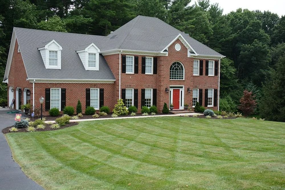 Two-story brick house with manicured lawn and trees in the background