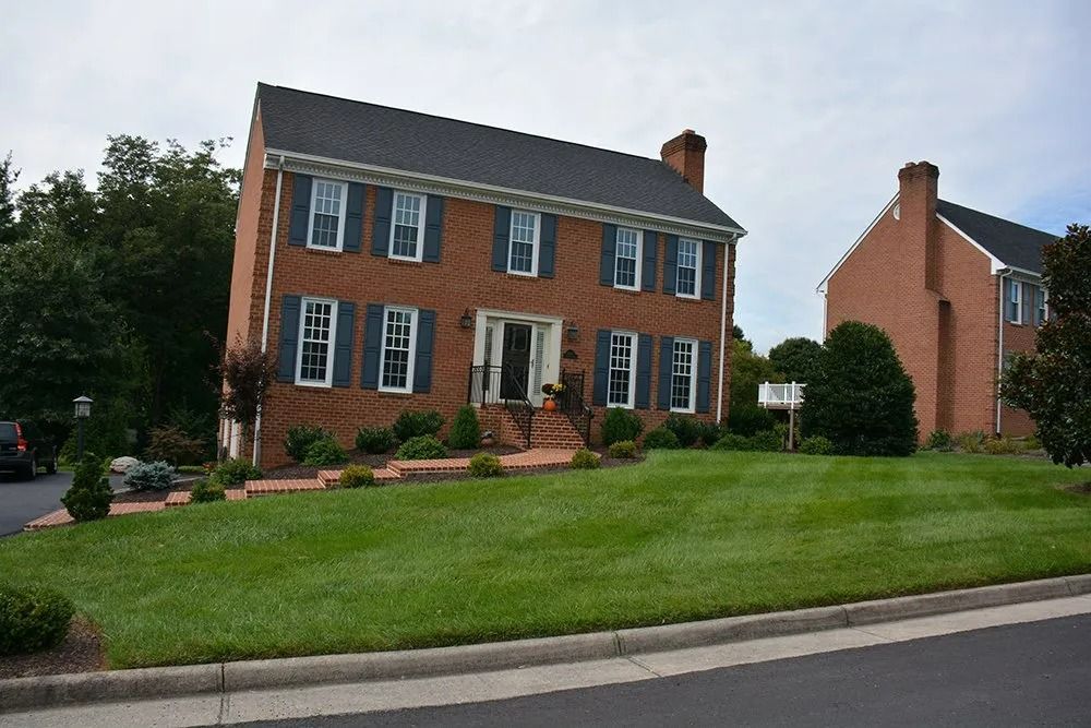Brick two-story suburban house with green lawn and shrubs beside a street