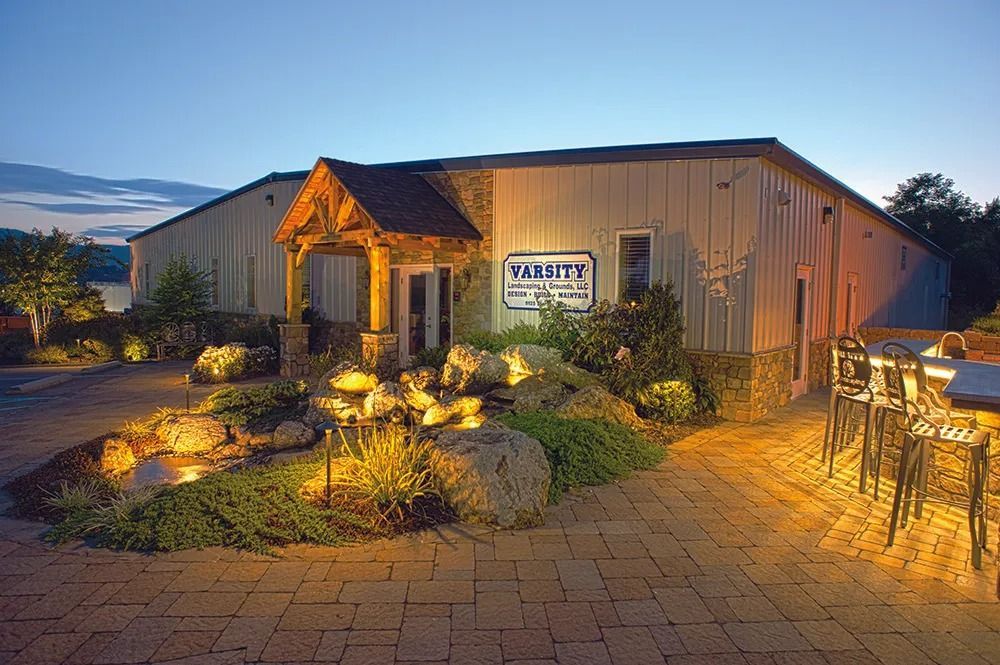 Illuminated barn-style venue with stone path, landscaped entrance, and outdoor tables at dusk