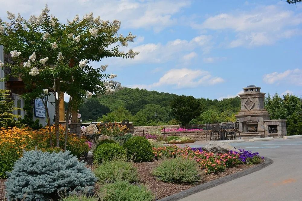 Garden beds with colorful flowers and shrubs beside a stone fireplace overlooking a landscaped hillside.