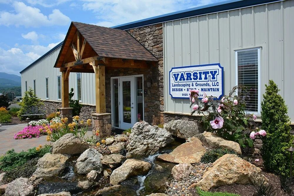 Varisty storefront with wooden entrance, rock landscaping, and flower beds under a clear blue sky