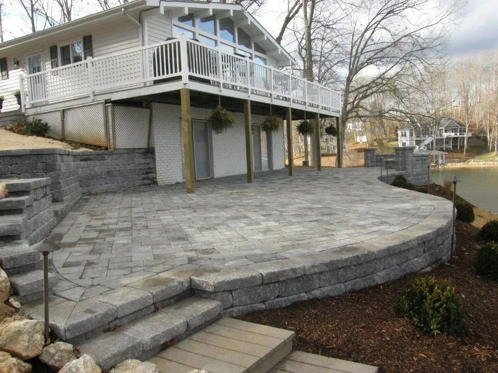 Stone patio and steps leading to a white house with a raised deck and railing.