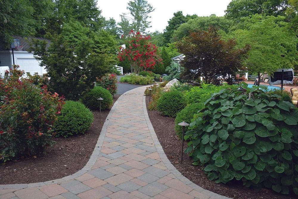 Curved stone path through a landscaped garden with shrubs, trees, and flowering plants