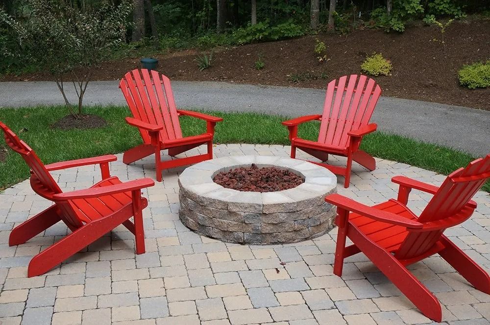 Four red Adirondack chairs around a stone fire pit on a paved patio outdoors