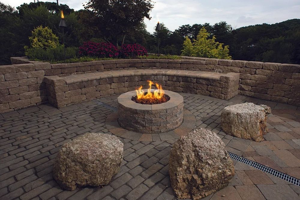 Stone patio with circular fire pit surrounded by rock seats in a landscaped backyard garden.