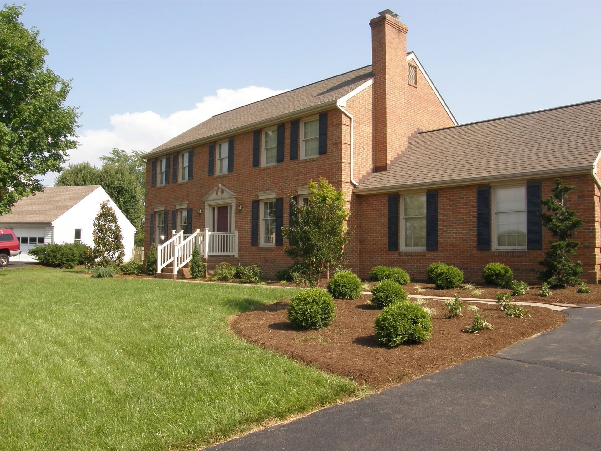 Brick suburban house with white trim, green lawn, and landscaped front yard beside a driveway