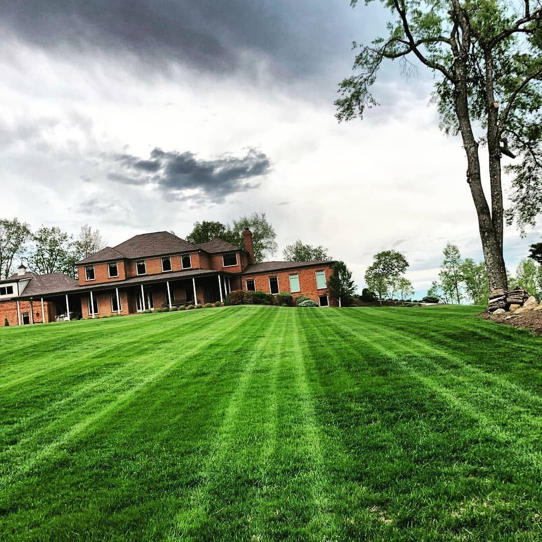 Wide green lawn leading to a rustic brick house under a cloudy sky