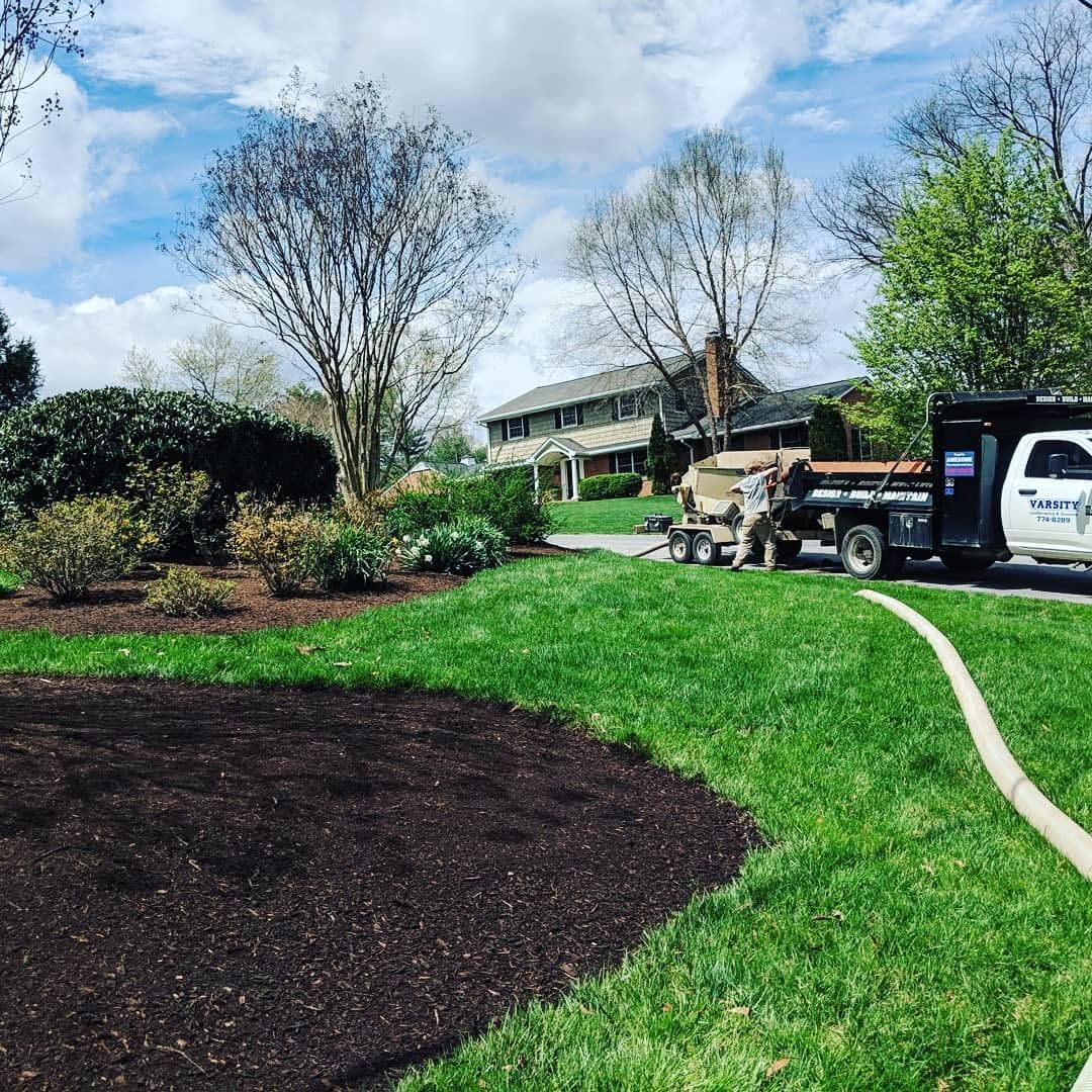 Landscaped yard with fresh mulch, green lawn, trees, and a work truck by a house under a cloudy sky