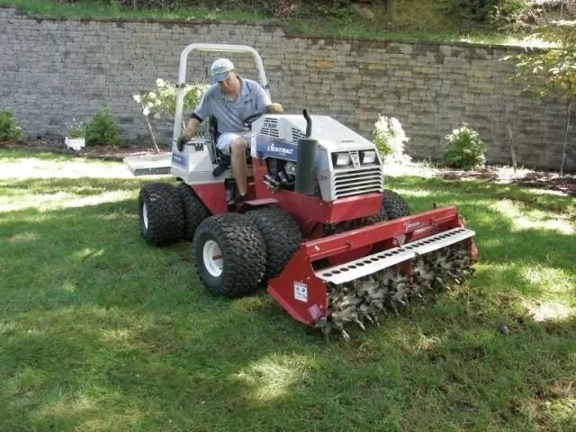 Man mowing grass on a red ride-on tractor with a front brush cutter in a yard